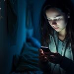 Ung person använder en smartphone i ett mörkt rum med blå belysning